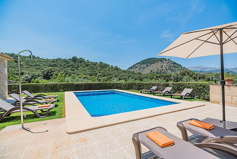 Sonnenschirm am Poolbereich vor der Finca mit Rasenfläche und Sonnenliegen