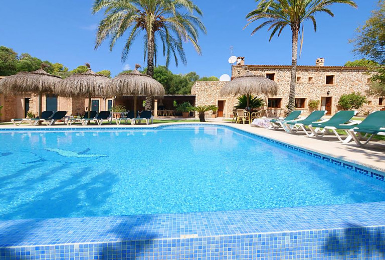 Pool mit Palmen und Sonnenschirmen vor dem Ferienhaus