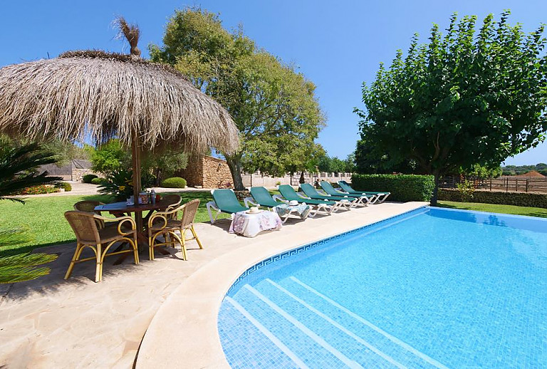 Rasen am Pool mit Sonnenliegen und Sonnenschirmen vor dem Ferienhaus